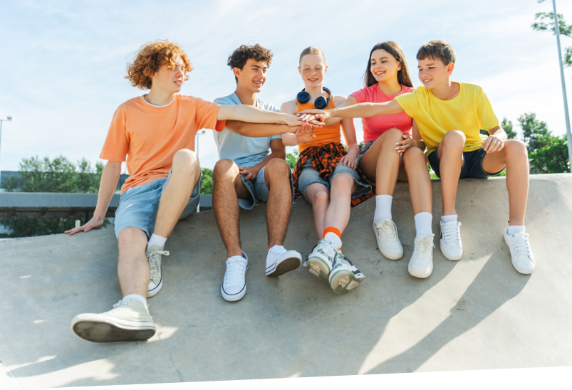 Excited multiracial friends, teenagers connecting hands, demonstrating spirit of friendship, sitting outdoors. Happy stylish boys and girls communication on the street. Positive lifestyle, summer