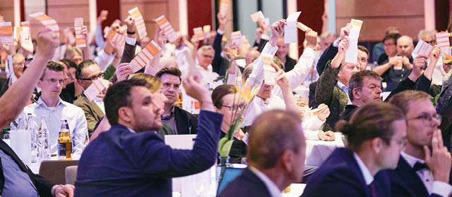 Eine gro e Personenmenge sitzt an Tiaschen in einem Saal. Die meisten heben eine Hand, in der sie ein wei es Papierblatt halten zur Abstimmung. Foto: Dethard Hilbig