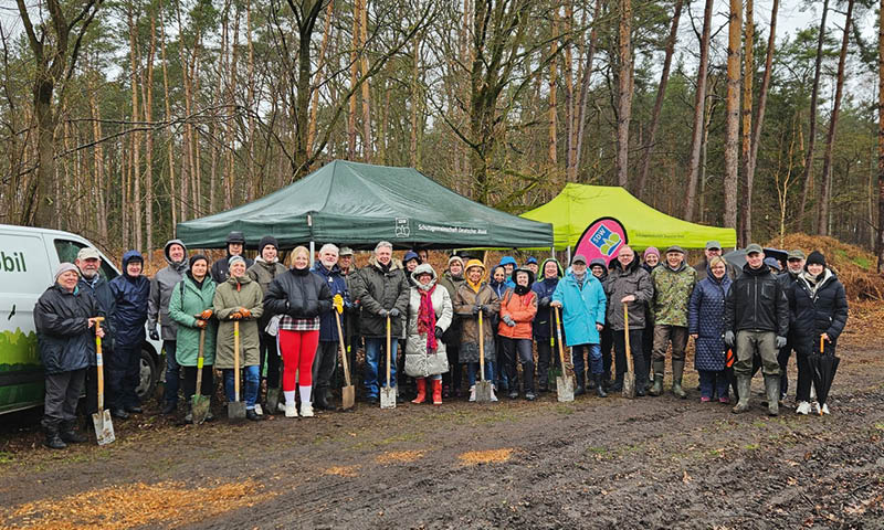 Bei k hlem, feuchten Winterwetter stehen eine gr ere Gruppe von Personen mit wetterfester, warmer Kleidung vor zwei Pavillons mit der Aufschrift “Schutzgemeinschaft deutscher Wald" auf einer Waldrodung. Der Boden ist matschig. Einige haben einen Spaten.  Foto: Hannoversche Volksbank