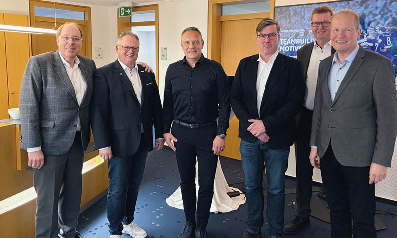 Sechs Herren in Hemden und Sakkos stehen in einem Raum vor einem Holztresen. Der dritte von links ist Andr Breitenreiter mit schwarzem Hemd und schwarzer Hose.  Foto: Hannoversche Volksbank